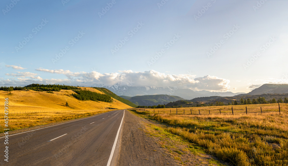 the road goes to the horizon to the mountains through the pass, the hills are covered with yellowing grass, the sun goes down to sunset, a journey through the mountainous Altai of Russia