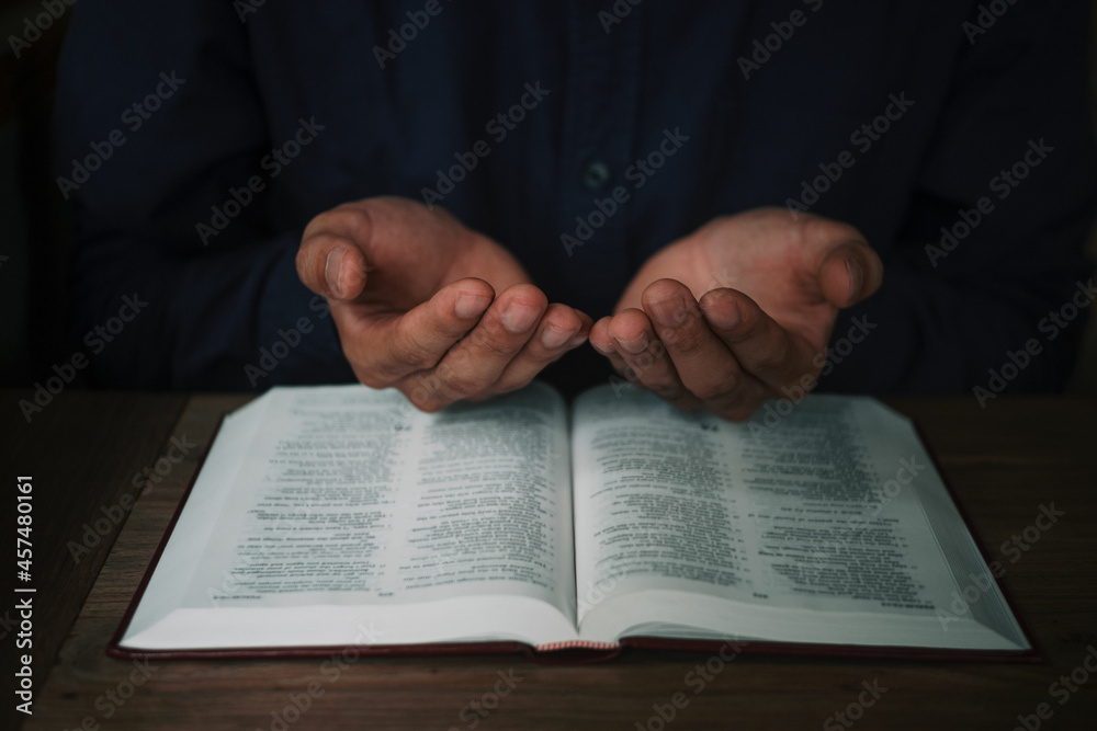 Man is reading and praying the scripture or holy bible on a wooden table with copy space. Religion, believe Concept.