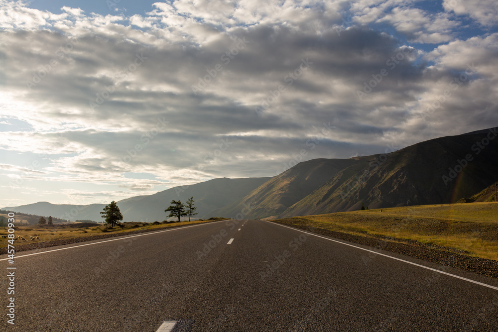Fototapeta premium road leading to the mountains and sunset with the sky covered with clouds