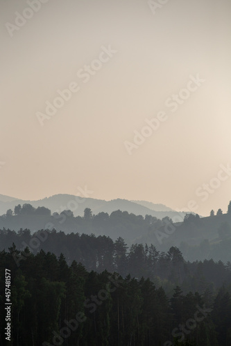 mountains overgrown with forests in a muddy haze by a road at different heights with multi-colored layers 