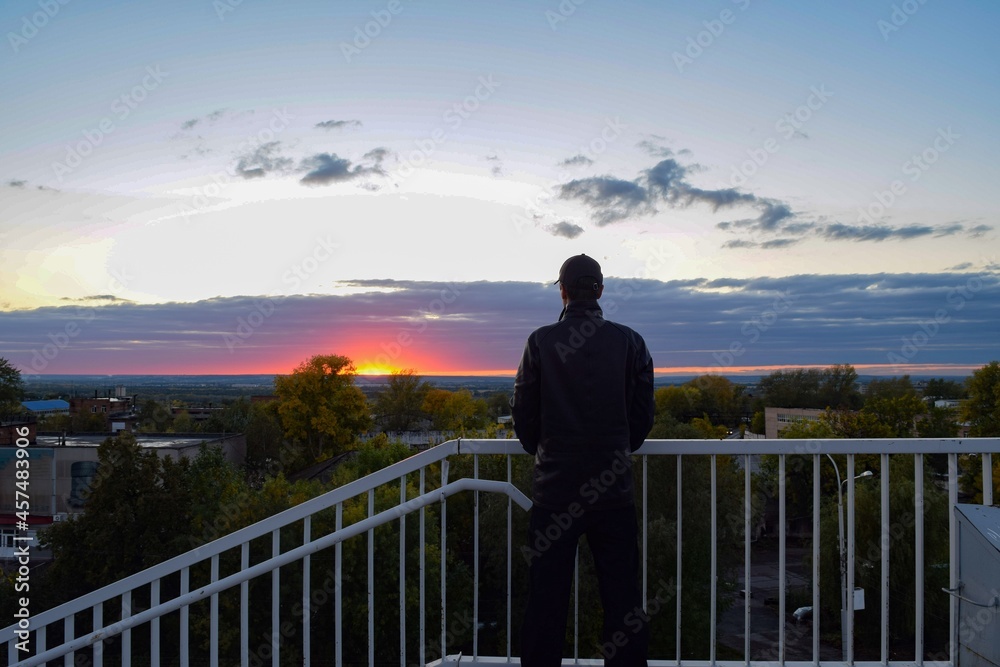 
The silhouette of a man who looks at the autumn orange sunset from the bridge
