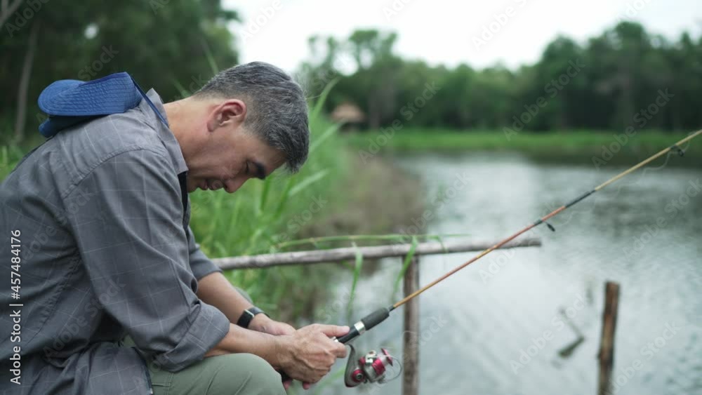Elderly Asian man, gray hair, hat, holding a fishing rod, sits and sleeps fishing. On the edge of the lake, on vacation, retirement, hobbies for the elderly, concept Elderly Asian man, gray hair, hat, holding a fishing rod, sits and sleeps fishing. On the edge of the lake, on vacation, retirement, hobbies for the elderly, concept