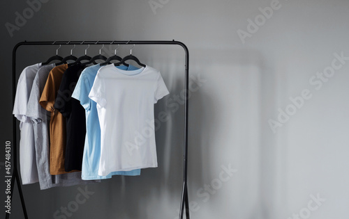 T-shirts of neutral colors on black hanger against gray wall
