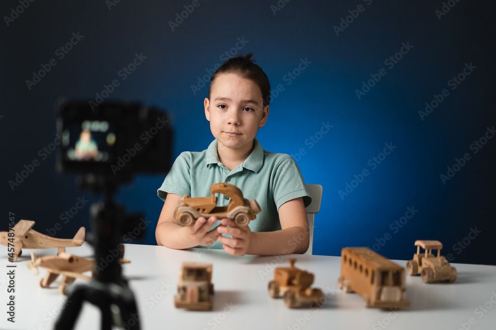 Kid blogger filming video on camera indoors with blue light in background. Online reviewing. Promoting eco wooden toys. Kid recording his gameplay for vlog. Kid blogger filming video on camera indoors with blue light in background. Online reviewing. Promoting eco wooden toys. Kid recording his gameplay for vlog.