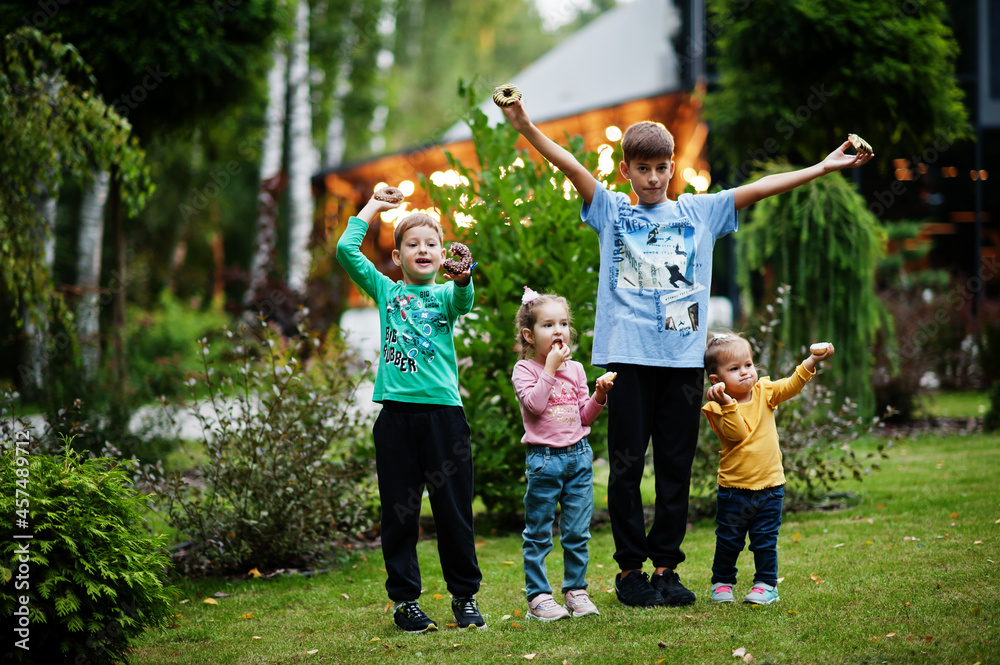 Obraz premium Four kids with doughnuts at evening yard. Tasty yummy donut food.