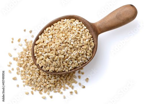 raw steel cut oats in the wooden spoon, isolated on the white background, top view