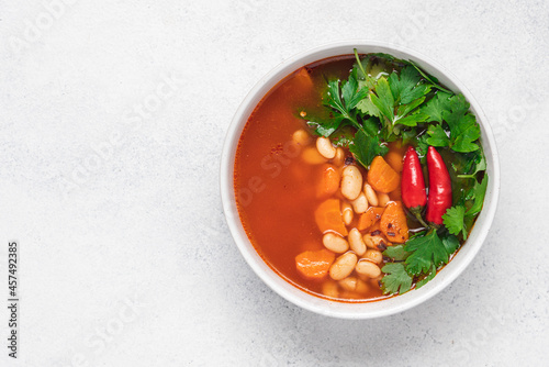 Vegetarian bean soup with tomato, hot peppers and green parsley. White background, top view