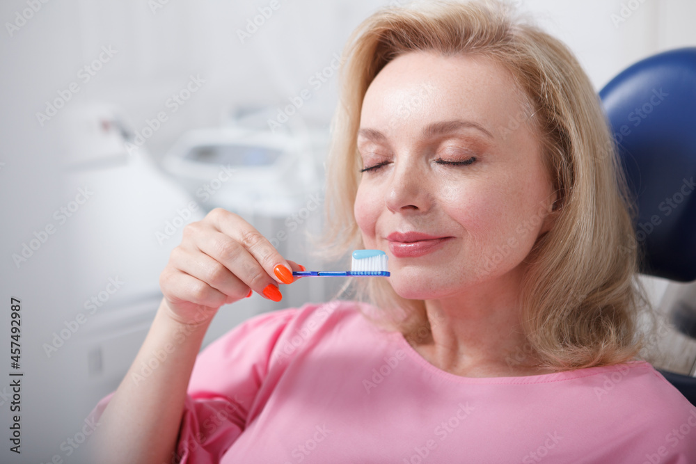 Mature woman smelling toothpaste on her toothbrush Mature woman smelling toothpaste on her toothbrush