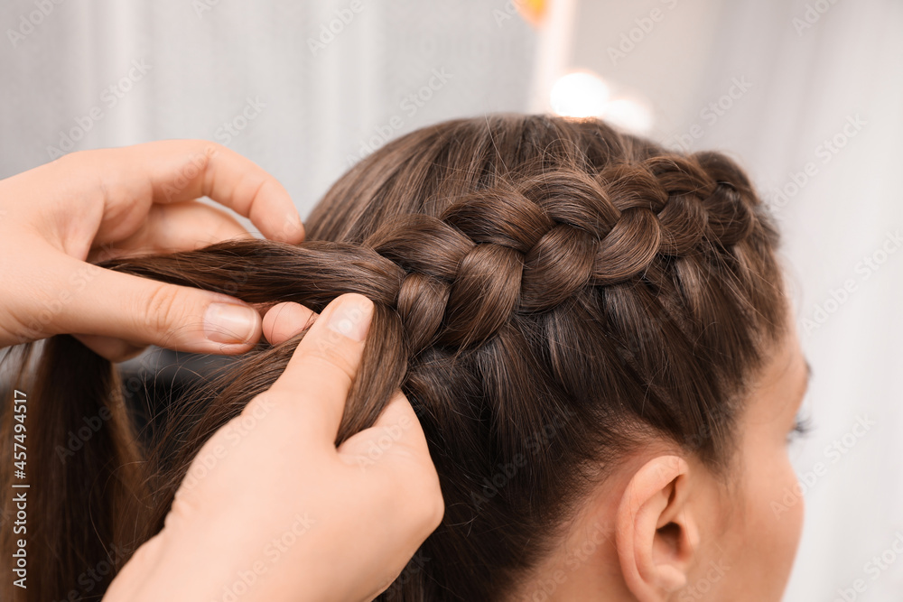 Naklejka premium Professional stylist braiding client's hair in salon, closeup