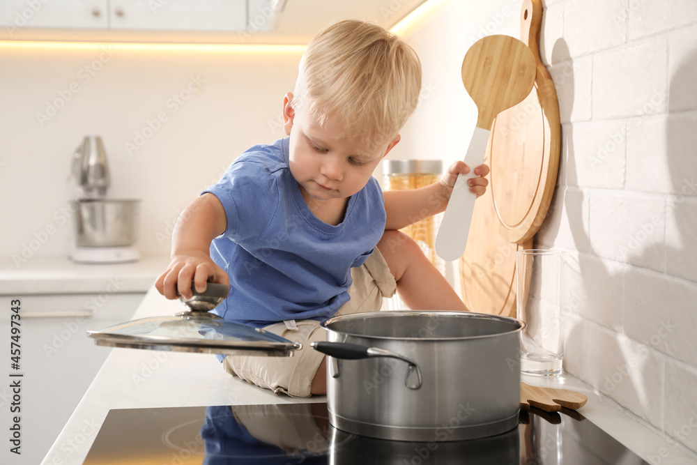 Curious little boy playing with pot on electric stove in kitchen Curious little boy playing with pot on electric stove in kitchen