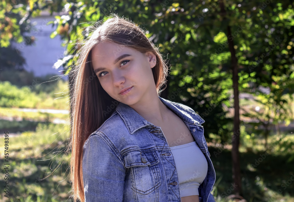 cute young beautiful teenage girl with long brown hair stands in the park against a background of green trees, her head thrown back cute young beautiful teenage girl with long brown hair stands in the park against a background of green trees, her head thrown back