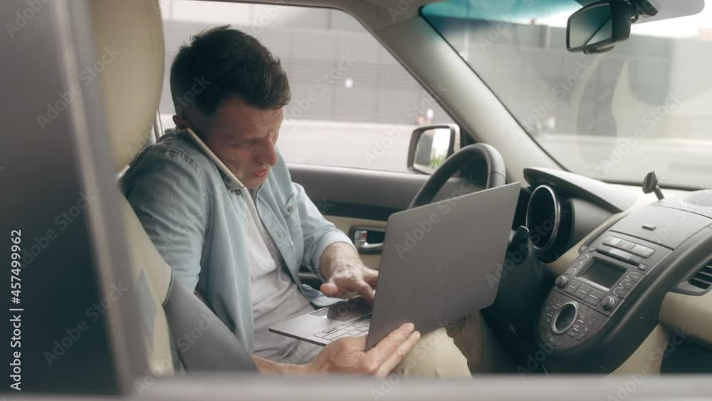 Busy businessman working on laptop, talking on phone in the car, online project