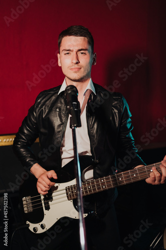 Talented handsome young guitarist man singing a song in studio recording on red background surrounded by instruments. Passion  hobby  singer  electric guitar