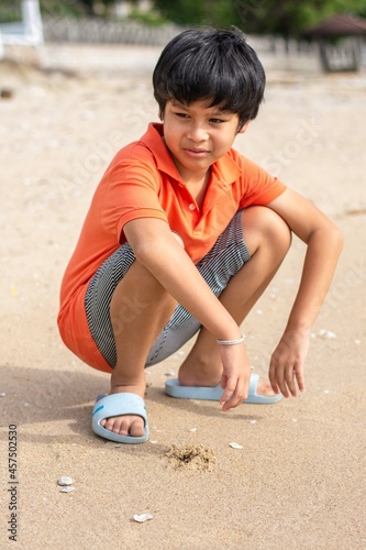 Portrait Asian boys wearing an orange shirt sitting on the beach