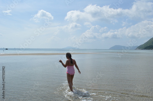 Little girl in pink swimsuit walking into the beach oh Con Dao, Vietnam