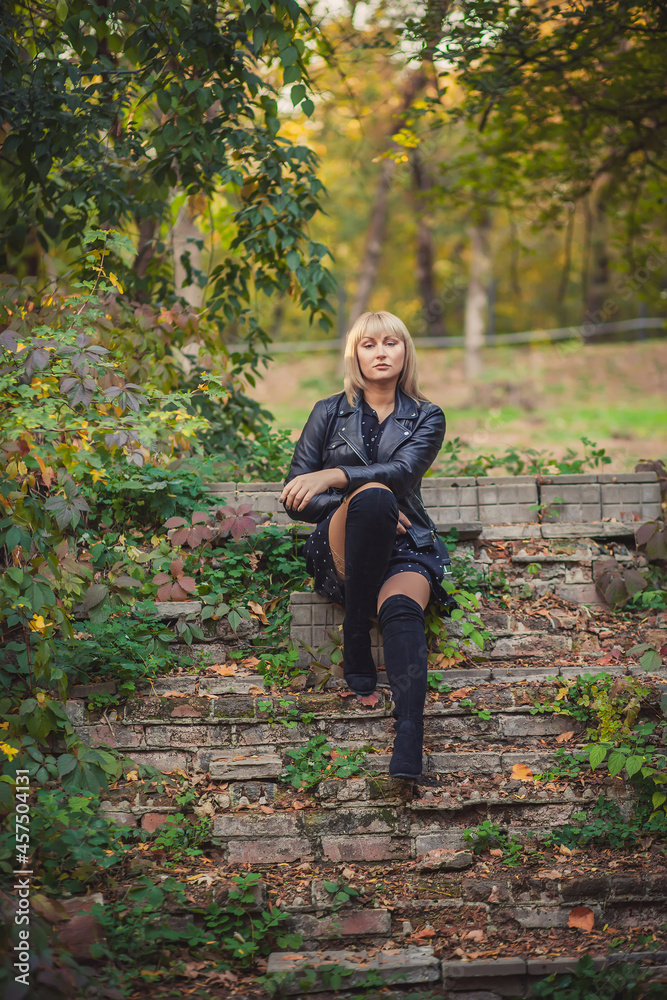 Woman with bob haircut in black leather jacket and high jackboots is sitting on an abandoned staircase in autumn Woman with bob haircut in black leather jacket and high jackboots is sitting on an abandoned staircase in autumn