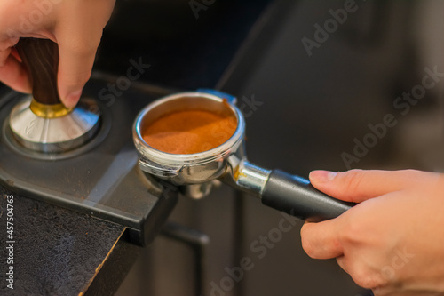 Man is using a tamper to press freshly ground morning coffee into a coffee tablet