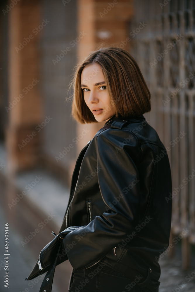 Young woman in sunglasses, hat and black leather jacket posing outdoor. Young woman in sunglasses, hat and black leather jacket posing outdoor.