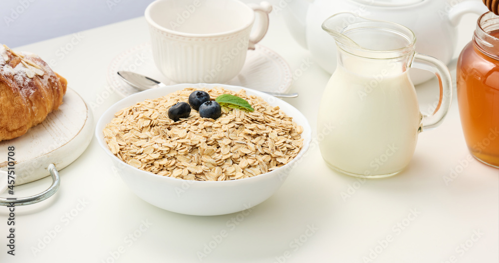 Raw oatmeal in white ceramic plate on white table, breakfast, close up Raw oatmeal in white ceramic plate on white table, breakfast, close up