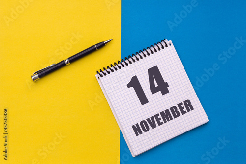 November 14th. Day 14 of month. Calendar date. Notebook with a spiral and pen lies on a yellow-blue background
