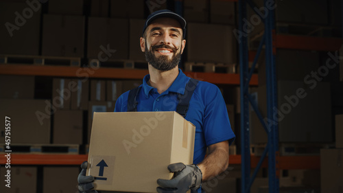 Portrait of Handsome Latin Male Worker Holding Cardboard Box Standing in Warehouse full Goods. Happy Professional Working in Logistics Distribution Center, Delivering e-Commerce Online Orders.