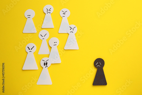 Black paper pawn standing out from white ones on yellow background, flat lay. Concept of racism photo