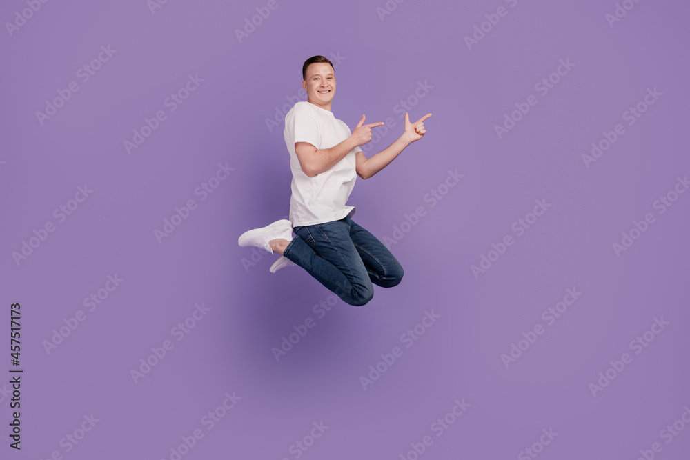 Portrait of excited dreamy positive guy jump direct fingers empty space on violet background
