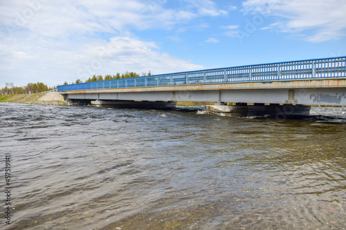 A concrete bridge for cars across a forest river on a sunny spring day in northern Russia.