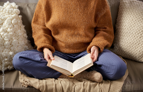 people, season and leisure concept - close up of woman in warm sweater reading book at home
