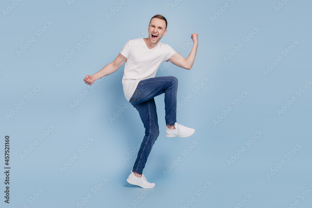 Full size photo of young cheerful man happy positive smile celebrate win victory champion fists hands isolated over blue color background Full size photo of young cheerful man happy positive smile celebrate win victory champion fists hands isolated over blue color background