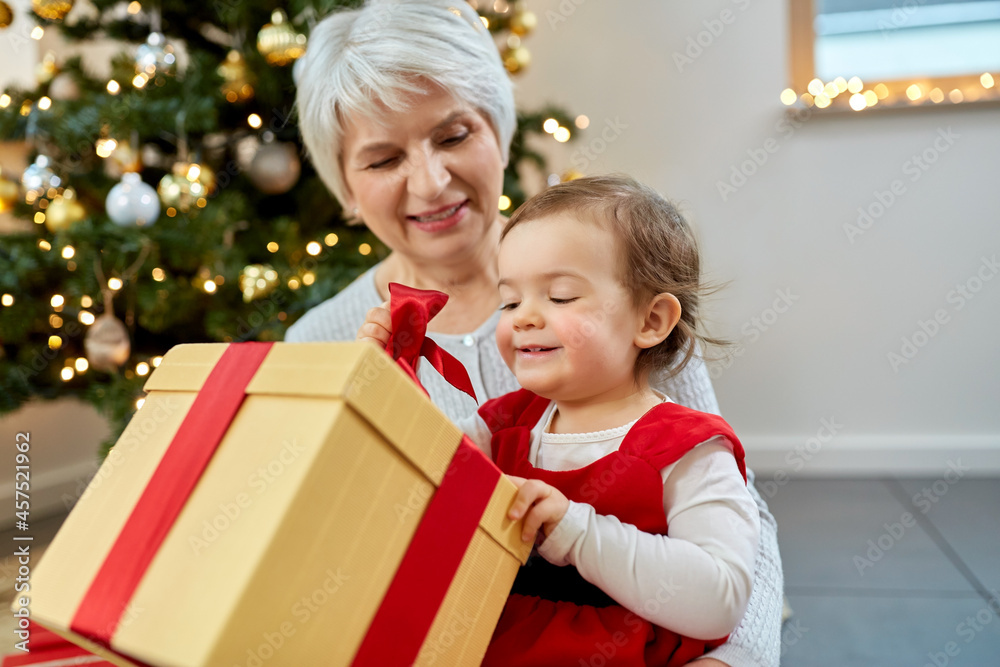 christmas, holidays and family concept - happy grandmother and baby granddaughter opening gift box at home