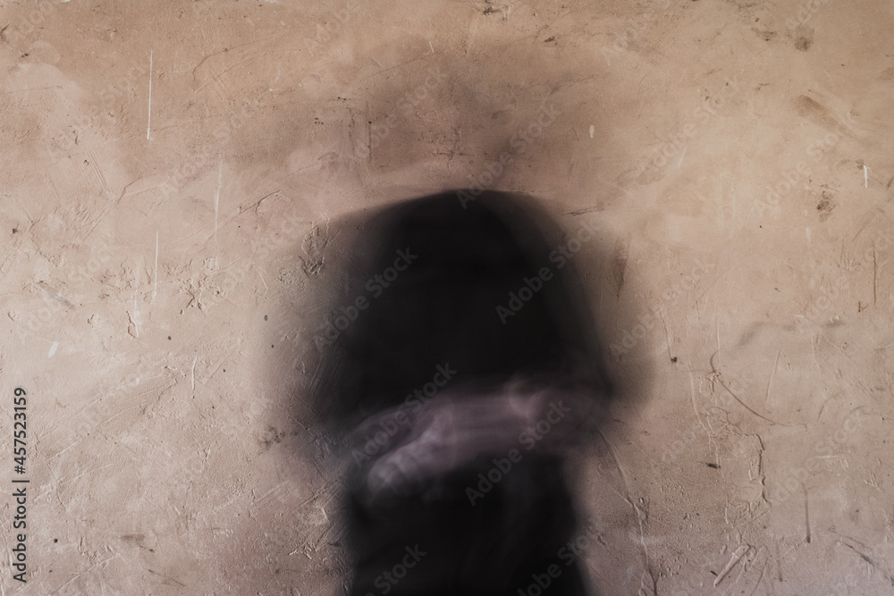 A blurred, ghostly figure with no head. Standing in front of a textured wall.