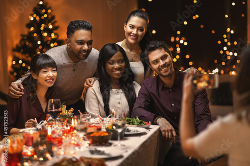 holidays  party and celebration concept - multiethnic group of happy friends having christmas dinner and photographing at home