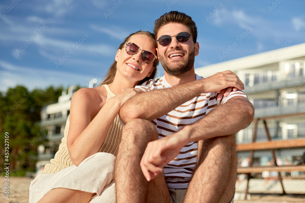 Fototapeta premium leisure, relationships and people concept - happy couple in sunglasses sitting on summer beach