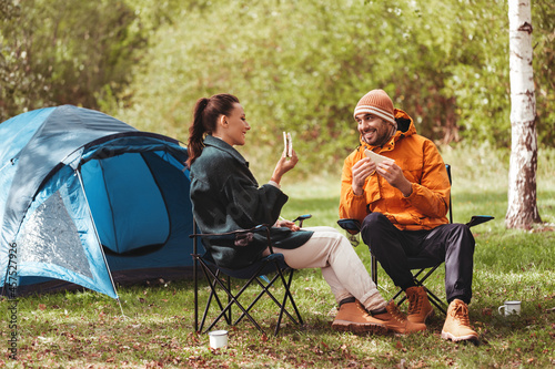 camping, tourism and travel concept - happy couple eating sandwiches at tent camp
