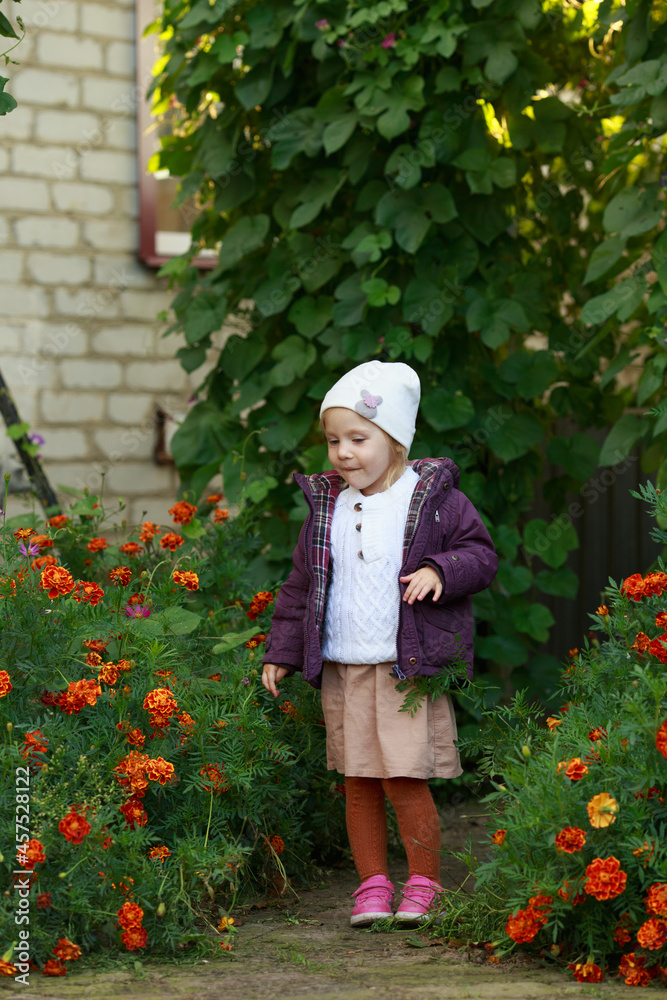 a little girl in a white hat, purple jacket, orange tights looks down and smiles
