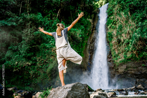 Woman standing in a yoga pose in front of a waterfall in the jungle