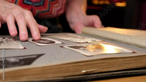 Elderly woman looks through an family album with old photos at table at home.