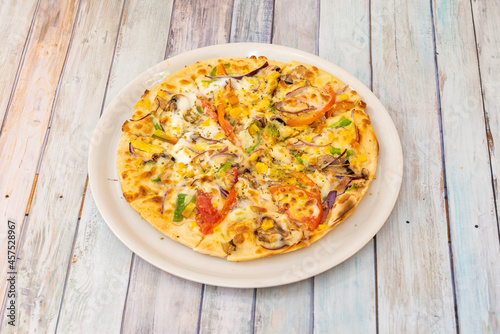 Vegetable pizza with potato cheese, sweet corn, red onion, crumbled tomato, red onion, slices of mushrooms and oregano