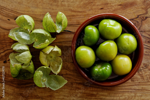 Husked tomatillos in clay bowl along with their husks lying on cutting board photo