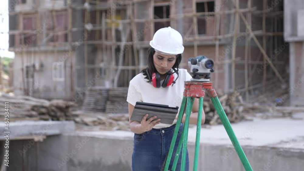 Construction female Worker Using Theodolite Surveying Optical Instrument for Measuring Angles in Horizontal and Vertical Planes on Construction Site.Worker in Hard Hat Making Projections using tablet. Construction female Worker Using Theodolite Surveying Optical Instrument for Measuring Angles in Horizontal and Vertical Planes on Construction Site.Worker in Hard Hat Making Projections using tablet.