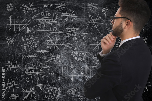 Young businessman in elegant suit near blackboard with drawn tic tac toe game