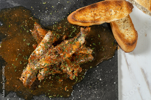 Close-up of a Appetizer served on a slab of sardines with tomato sauce and herbs with some toast bread.