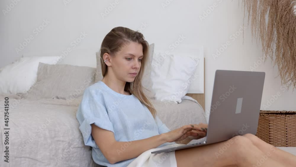 Blonde woman typing on keyboard, sitting on the floor in bedroom. Side view of busy attractive freelancer with device working at home, gimbal shot. Concept of remote work Blonde woman typing on keyboard, sitting on the floor in bedroom. Side view of busy attractive freelancer with device working at home, gimbal shot. Concept of remote work