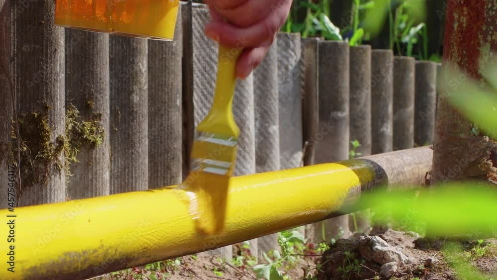 Stockvideo A hand paints a rusty pipe with a brush with yellow paint
