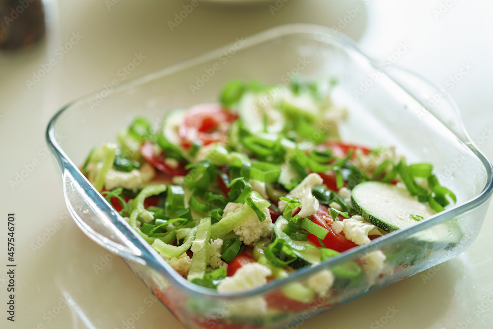 dish of fresh vegetables in a glass form stands on a wooden table in the kitchen. Vegetable casserole, zucchini, tomatoes Proper nutrition. Healthy weight loss.