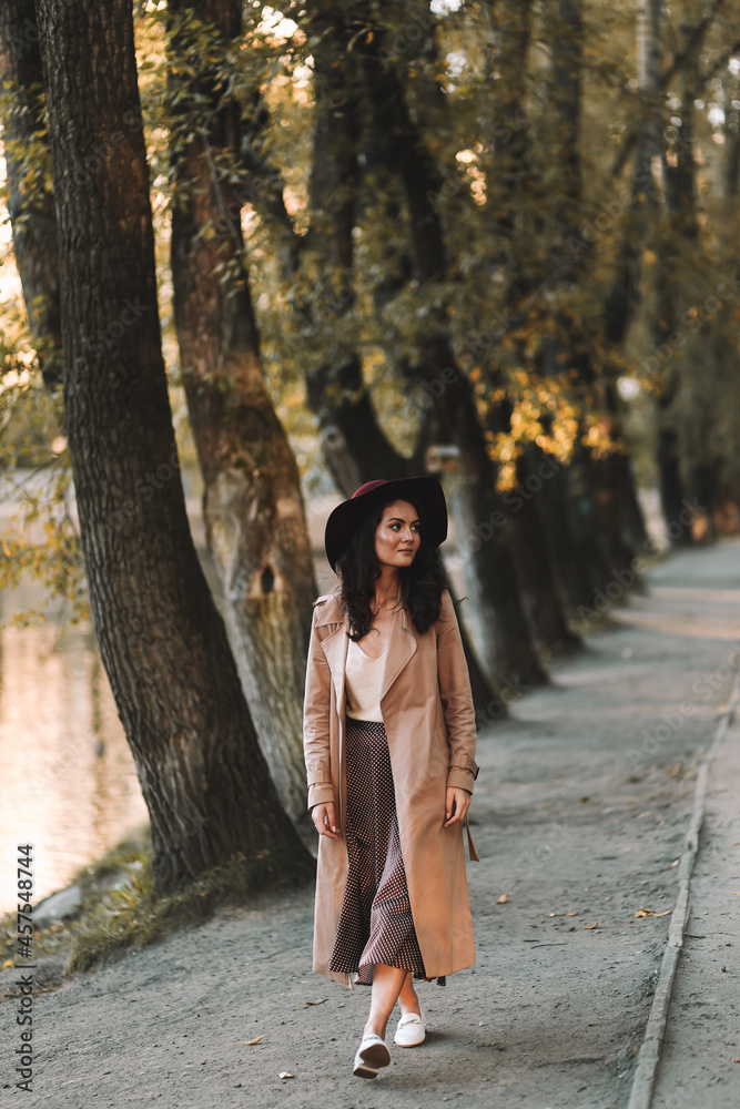 A pretty single woman in an elegant hat and stylish outerwear walks in an fall park among the trees enjoys solitude in nature in autumn outdoor, selective focus A pretty single woman in an elegant hat and stylish outerwear walks in an fall park among the trees enjoys solitude in nature in autumn outdoor, selective focus