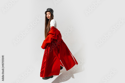 Fashion studio photo of stylish european brunette woman in red coat and black hat posing on white background.  Trendy winter accsesorises. Full lenght.