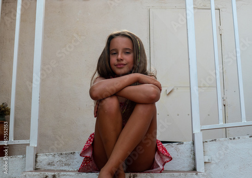 Cute teenage Caucasian smiling girl with long hair sitting on the stairs with legs and arms crossed