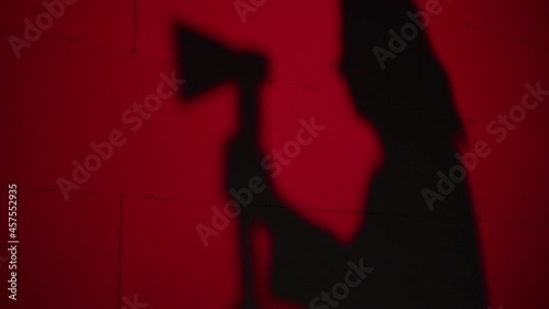 Creepy death silhouette running for victim with axe on red background. Mystical scary murderer, maniac catching up woman. Halloween costume of killer. Horror scene movie of psycho serial. 